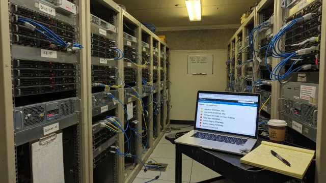 Server racks with blinking status lights and a laptop showing a build pipeline list
